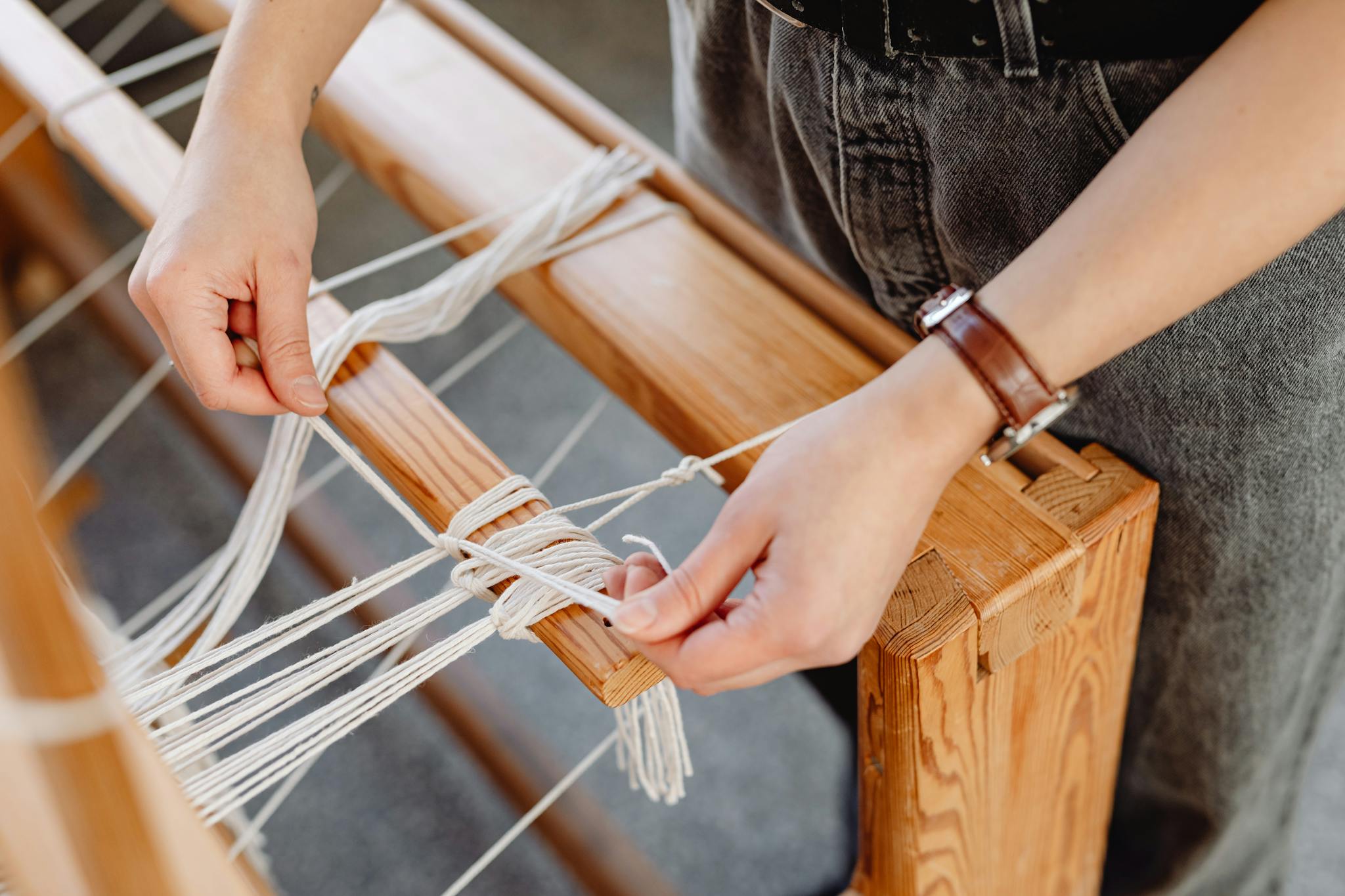 Detailed view of hands weaving fabric using a wooden loom, showcasing craft and artistry.